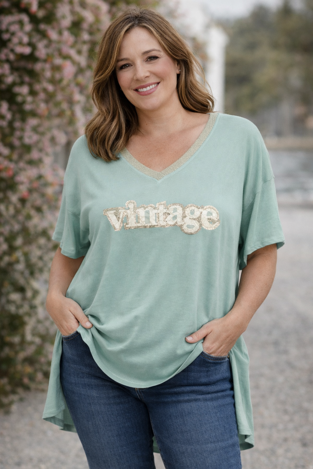 Femme en t-shirt vert d'eau “Vintage”, fond doux et fleurs floutées, ambiance féminine et simple.