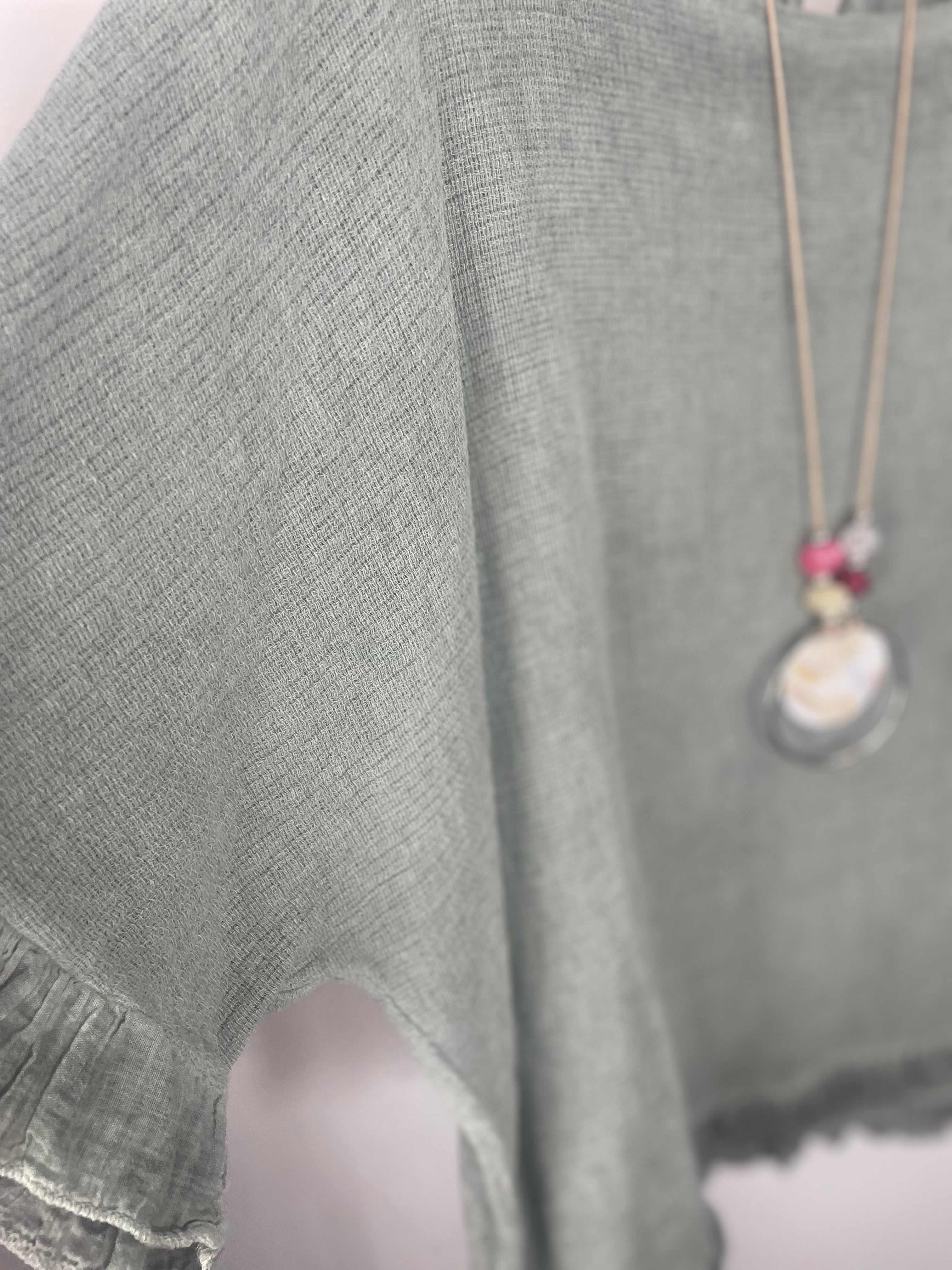 Détail textile gaufré et finitions froufrous sur blouse bohème avec collier sautoir perles.