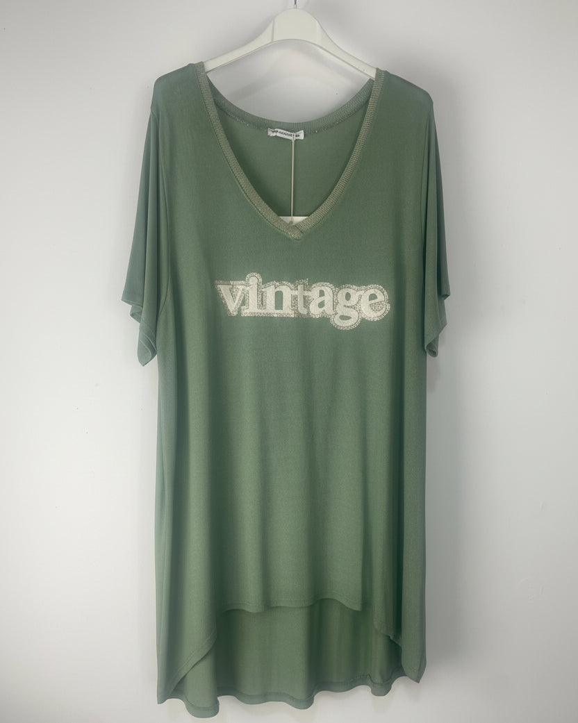 T-shirt kaki “Vintage” col V pailleté suspendu, lumière naturelle et déco murale bohème.