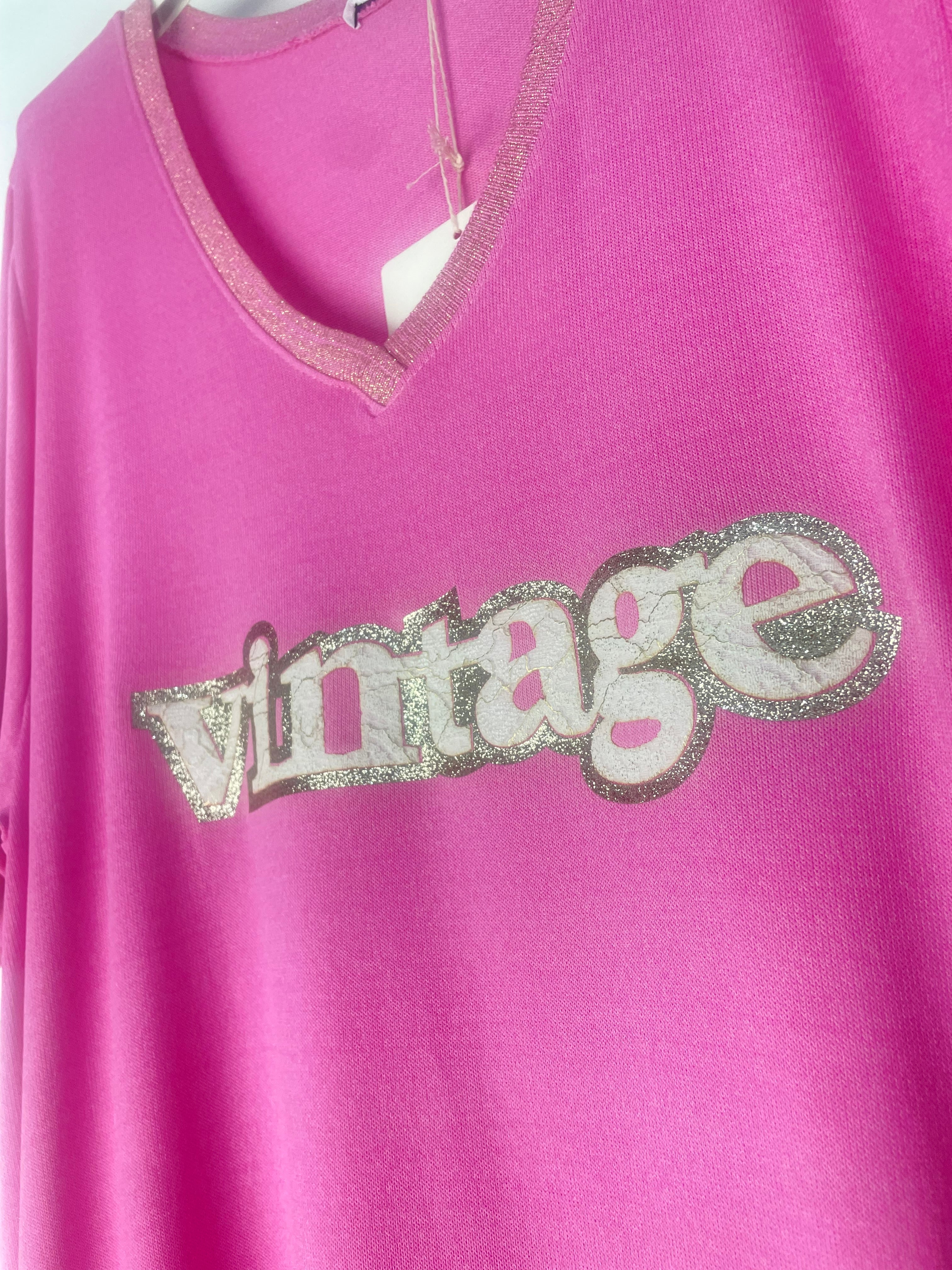 Détails inscription et col paillette T-shirt rose fuchsia “Vintage” à sequins dorés suspendu sur cintre blanc, fond mural neutre