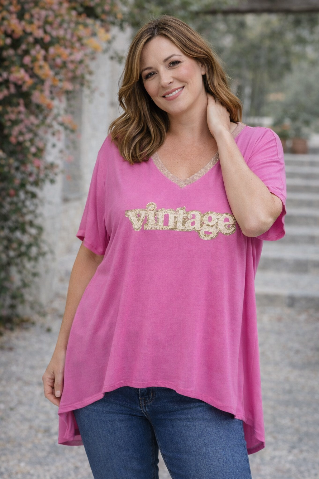 Femme blonde en t-shirt rose fuchsia “Vintage”, pose naturelle, fond flouté et lumière chaude.