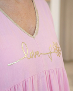 Gros plan sur la broderie dorée Love fleurie et le liseré pailleté du décolleté d'une blouse bohème rose.