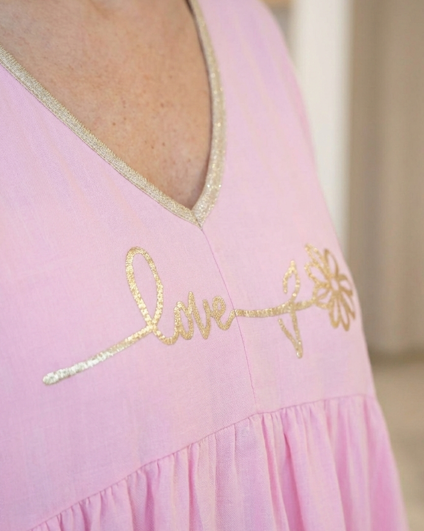 Gros plan sur la broderie dorée Love fleurie et le liseré pailleté du décolleté d'une blouse bohème rose.
