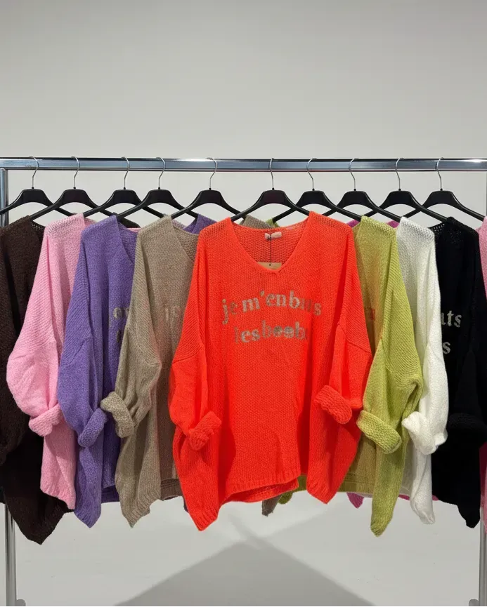 Rangée de pulls colorés “Je m’en bats les boobs” sur cintres.