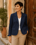 Femme portant le Blazer Siena en denim stretch bleu avec top blanc et pantalon camel devant une porte ancienne en Italie