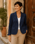 Femme portant le Blazer Siena en denim stretch bleu avec top blanc et pantalon camel devant une porte ancienne en Italie