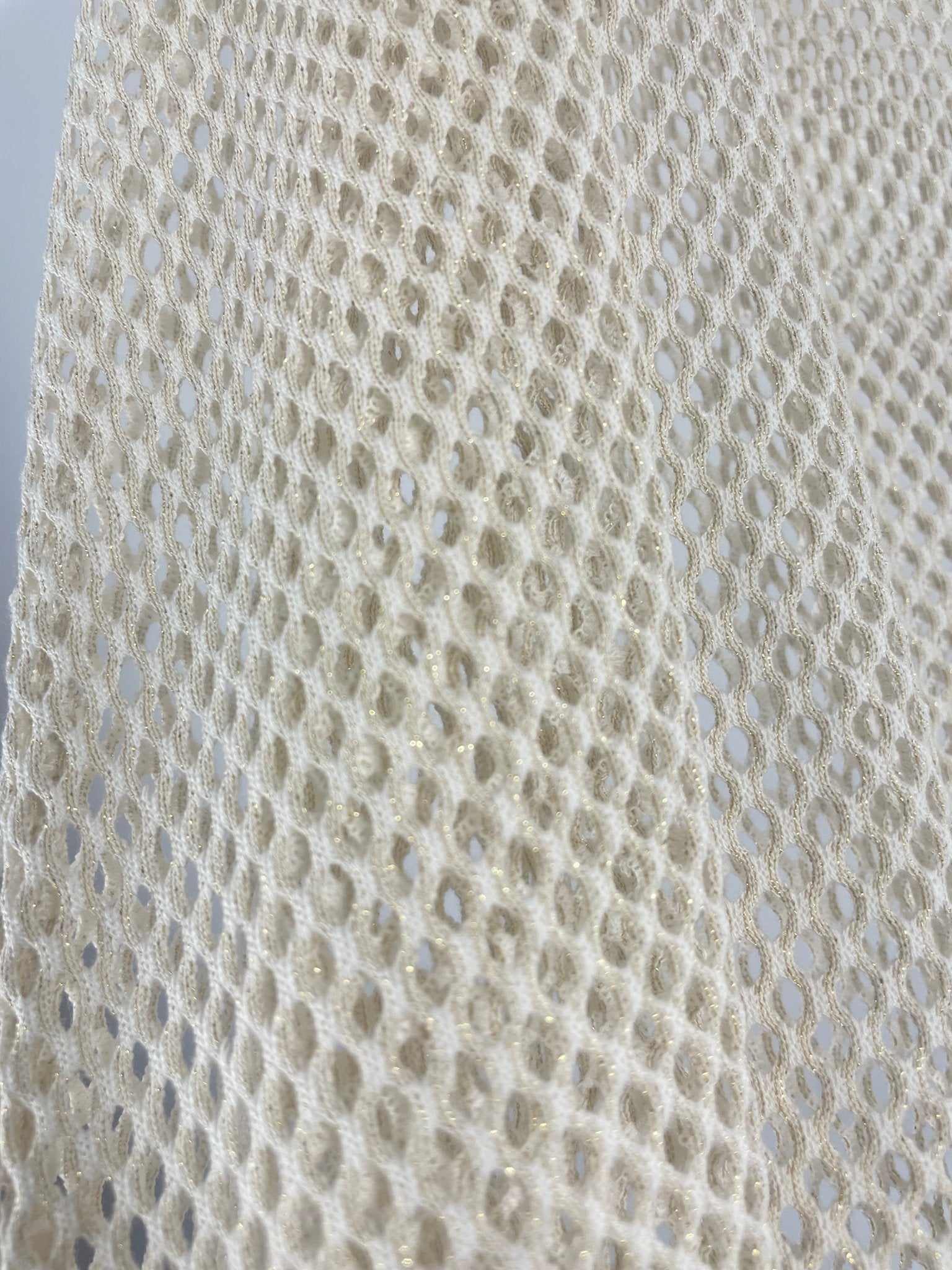 Gros plan sur la maille filet ajourée écru de la tunique bohème, fil lurex doré intégré visible en lumière naturelle, texture artisanale