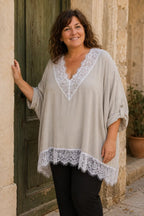 Femme portant la blouse Siena beige ample à dentelle blanche avec un pantalon noir devant une porte vert olive