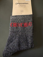 Détail des chaussettes CHOUCHOU noires, de leur maille pailletée et du message rouge.