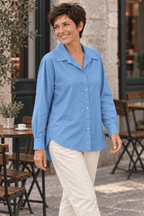 Chemise bleue en coton portée de trois quarts avec un pantalon écru à une terrasse de café.