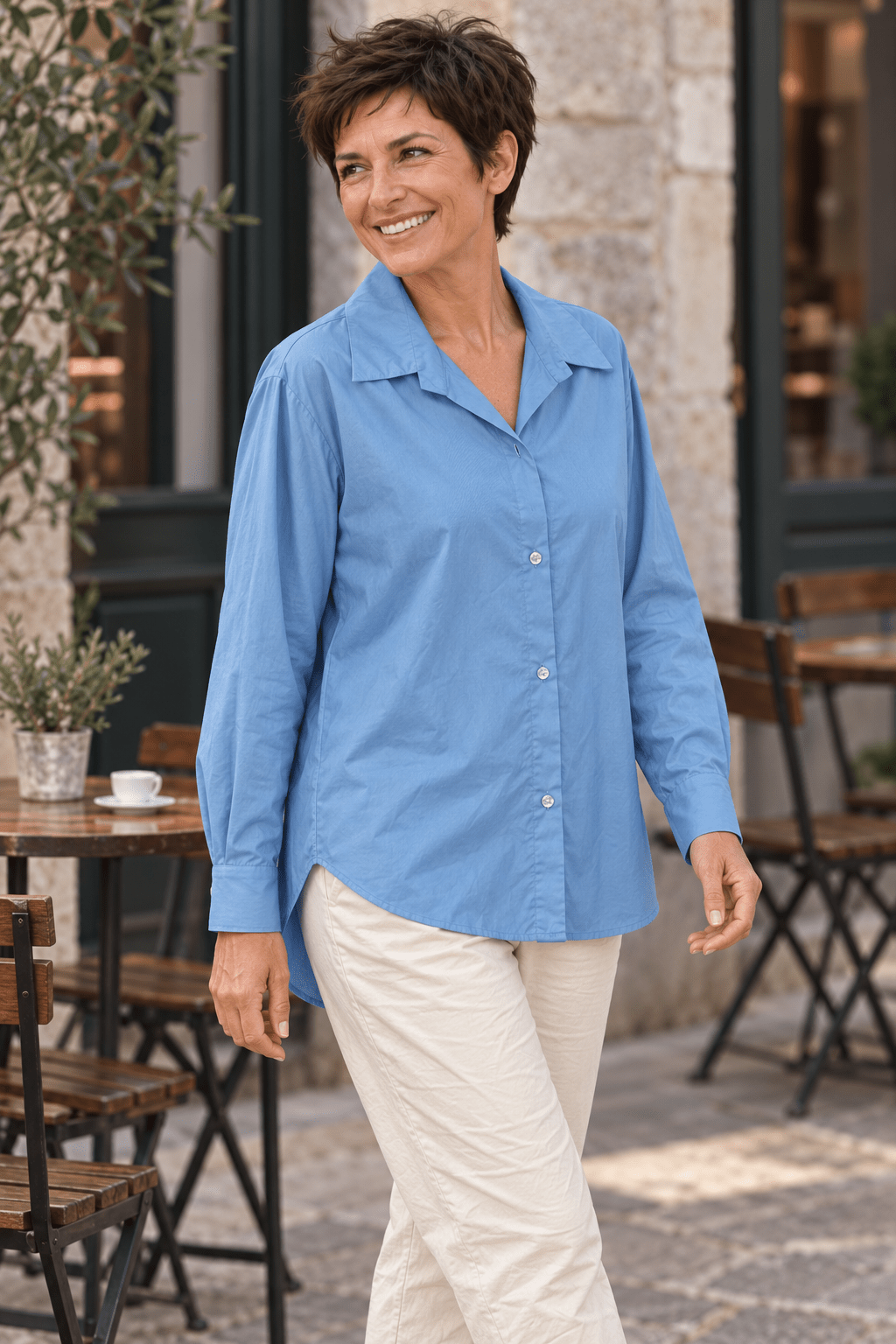 Chemise bleue en coton portée de trois quarts avec un pantalon écru à une terrasse de café.