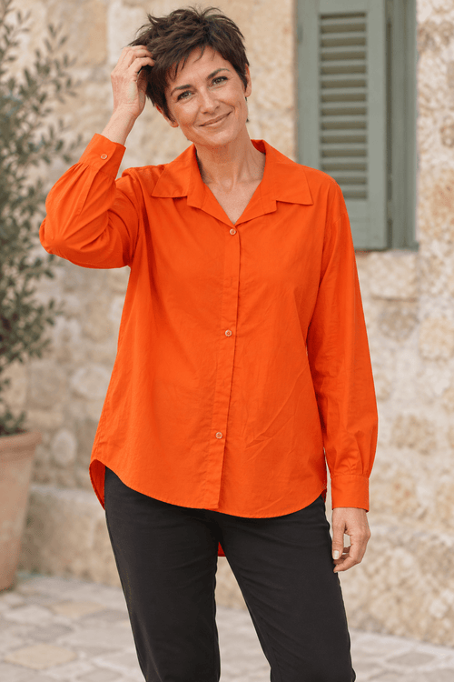 Chemise orange en coton à col ouvert portée sur un pantalon noir, bas de la chemise laissé libre.