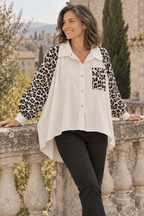 Chemise blanche trapèze à manches léopard portée avec un pantalon noir près d’une balustrade.