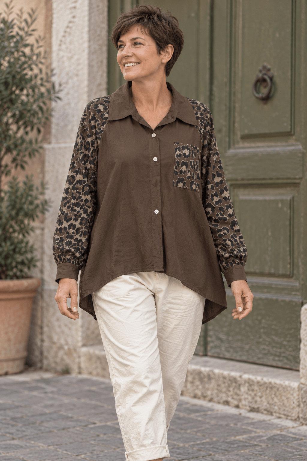 Chemise chocolat à manches léopard portée par une femme aux cheveux courts avec un pantalon écru.