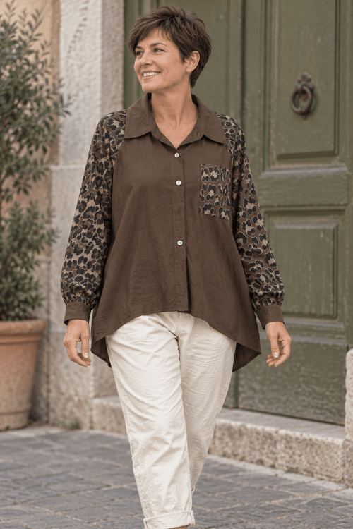 Chemise chocolat à manches léopard portée par une femme aux cheveux courts avec un pantalon écru.