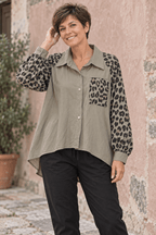 Femme aux cheveux courts portant la chemise taupe à manches et poche léopard avec un pantalon noir, devant un mur vieux rose.