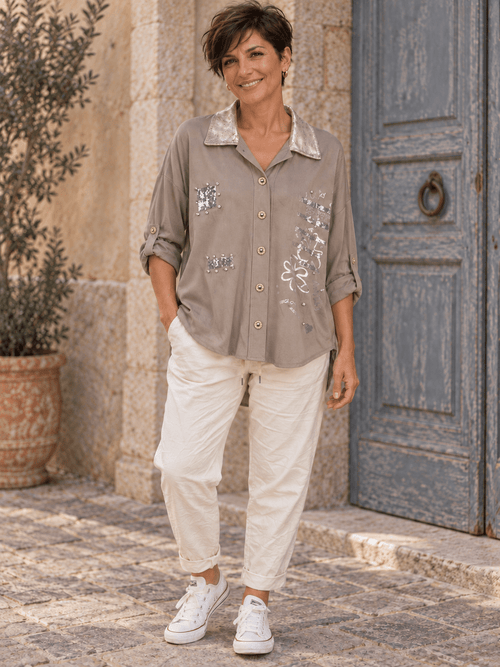 Tenue avec chemise taupe à col métallisé, cinq boutons décoratifs et pantalon écru.
