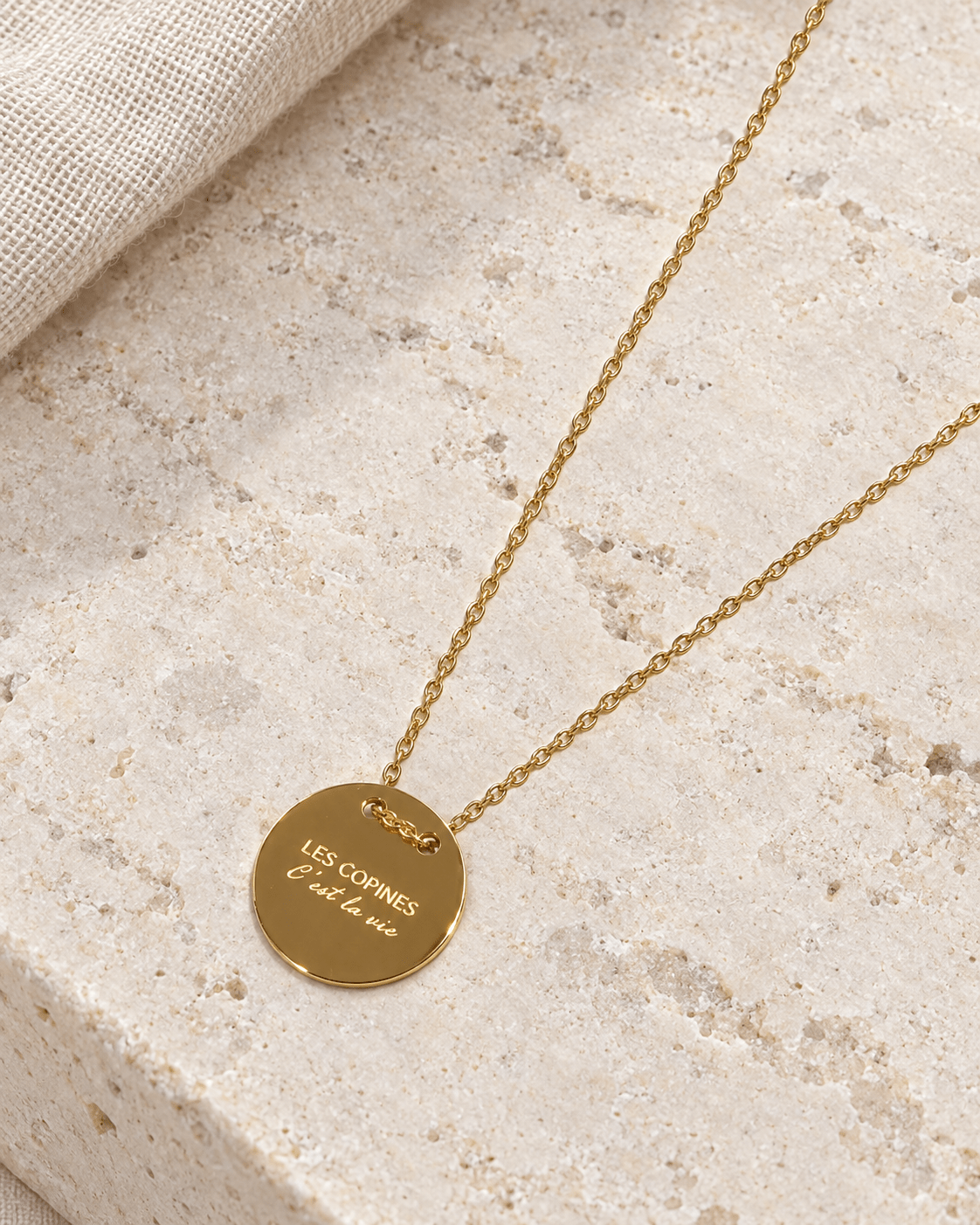 Vue retouchée du collier doré Les copines c’est la vie, gravure et chaîne sur pierre claire.