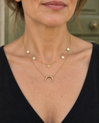Collier doré double rang porté au décolleté, cinq pastilles et croissant de lune.