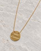 Vue retouchée de la médaille dorée Maman d’amour et de sa chaîne sur pierre claire.
