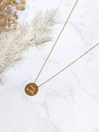Photo originale du collier doré Mamie en Or, médaille ronde sur fond blanc avec fleurs séchées.
