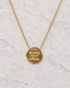 Vue retouchée de la médaille dorée Super tata et de sa chaîne sur pierre claire.