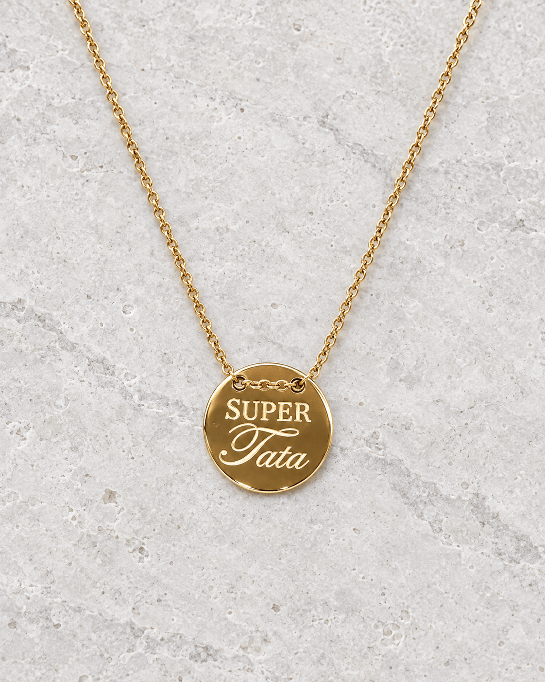 Vue retouchée de la médaille dorée Super tata et de sa chaîne sur pierre claire.
