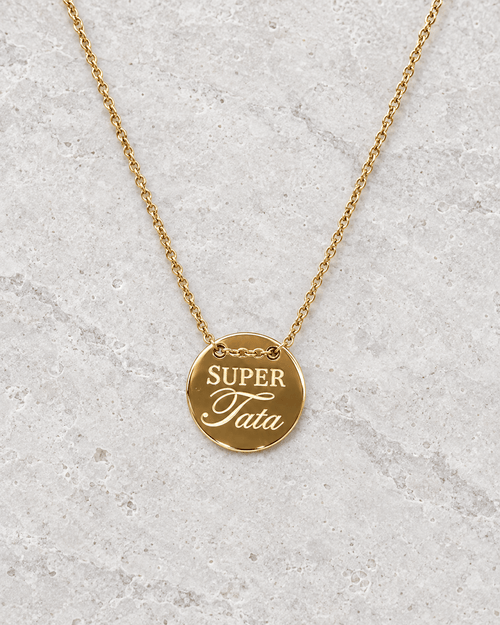 Vue retouchée de la médaille dorée Super tata et de sa chaîne sur pierre claire.