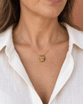 Collier doré Super tata porté au décolleté avec une chemise ivoire.