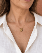 Collier doré Super tata porté au décolleté avec une chemise ivoire.