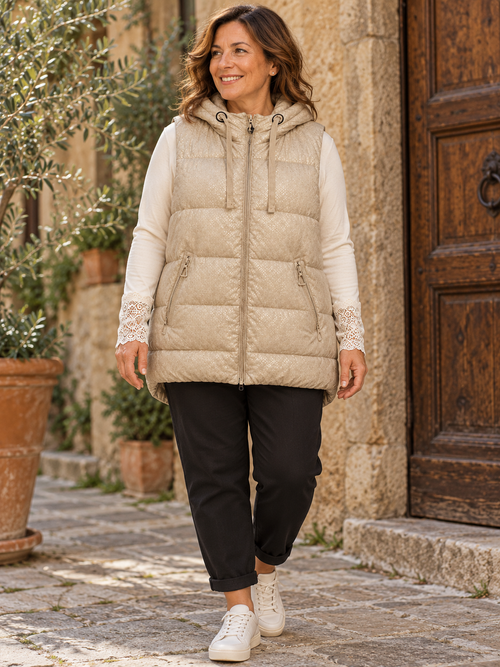 Femme portant la doudoune beige irisée à capuche, avec un haut écru à poignets dentelle et un pantalon noir