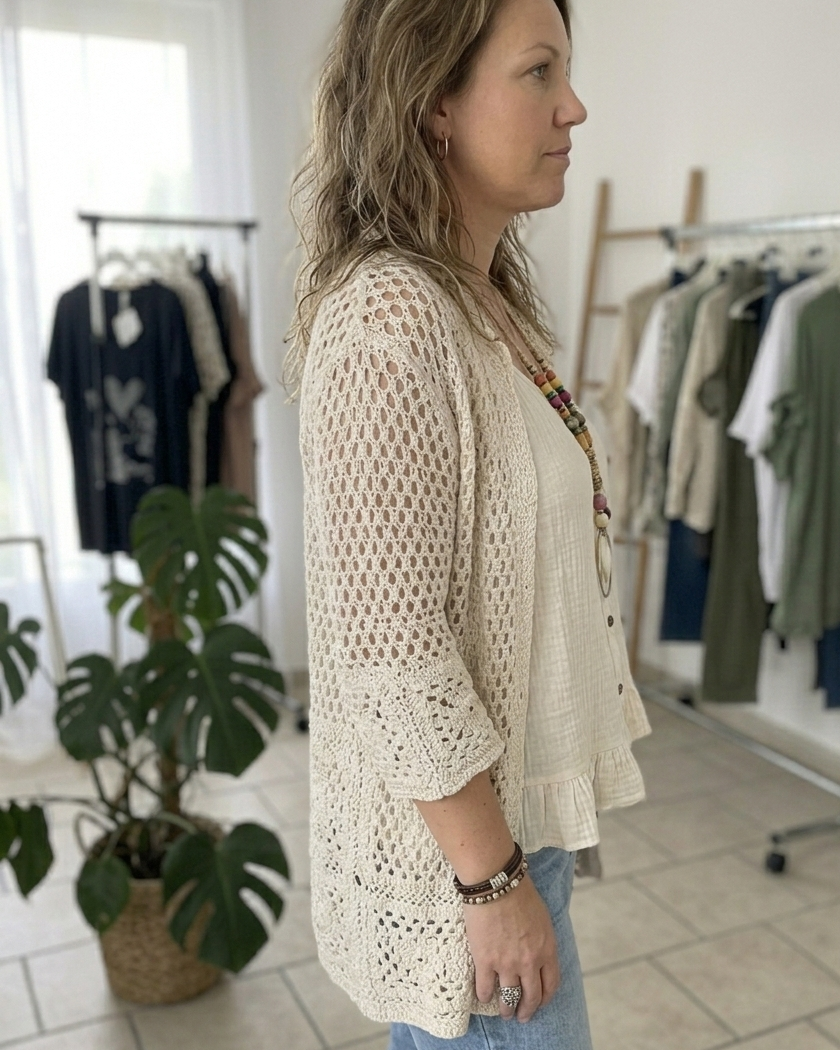 Vue de dos du gilet crème en crochet sur mannequin : détails maille complexe et fente latérale de la blouse verte.