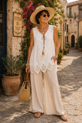 Femme portant un top bohème blanc brodé avec lien plume, pantalon fluide palazzo, chapeau d’été et accessoires naturels