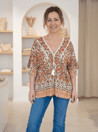 Femme portant une blouse bohème fluide à imprimé ethnique marron et orangé, coupe évasée sous la poitrine.