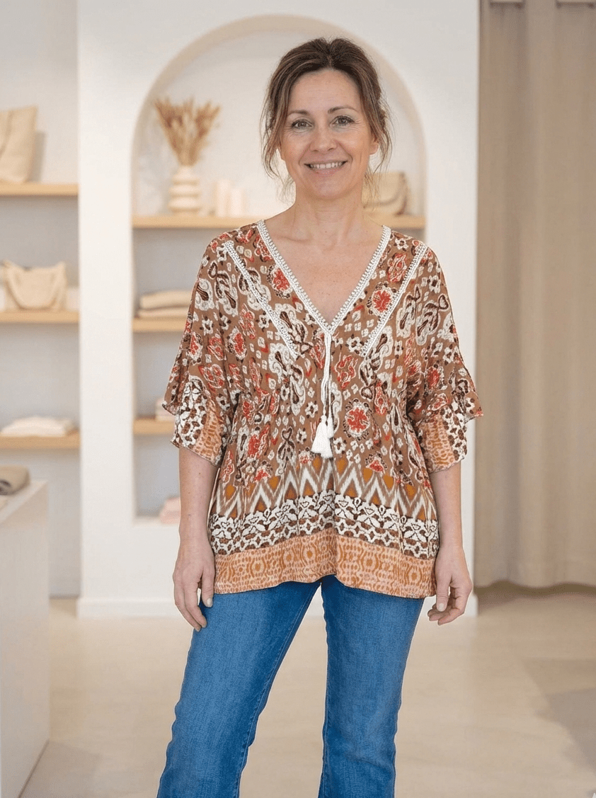 Femme portant une blouse bohème fluide à imprimé ethnique marron et orangé, coupe évasée sous la poitrine.