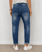 Vue portée de dos du jean Amore S.Woman en denim bleu avec poches arrière et effet délavé, baskets blanches à détails dorés
