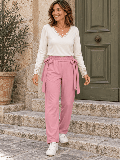 Tenue complète avec jogging rose poudré à nœuds sur les côtés, haut écru à dentelle et baskets blanches.