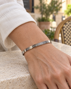 Bracelet jonc argenté Un jour, mon prince viendra porté seul au poignet, près d’une manche ivoire.