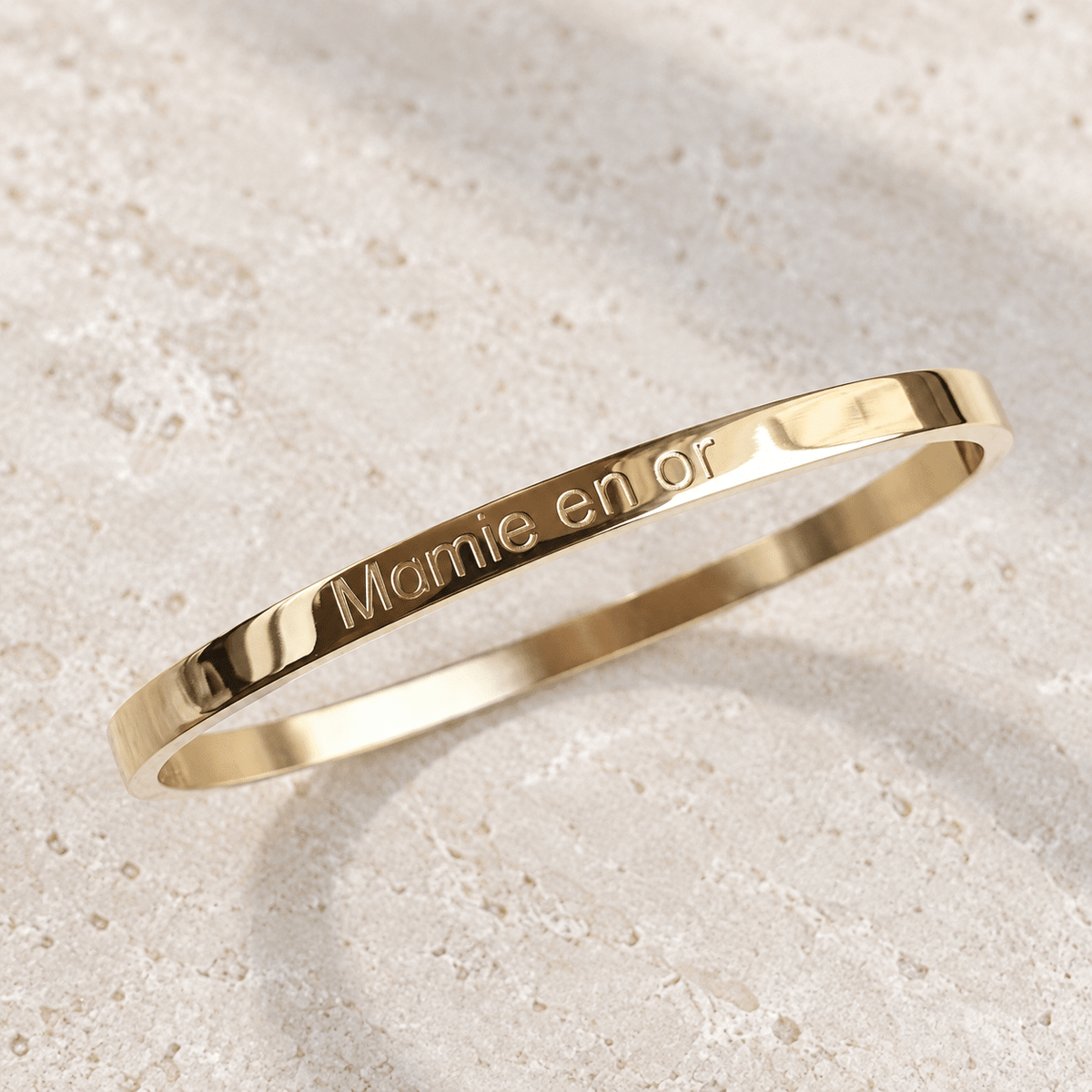 Bracelet jonc Mamie en or – Acier inoxydable doré sur pierre claire, vue du bijou retouchée.
