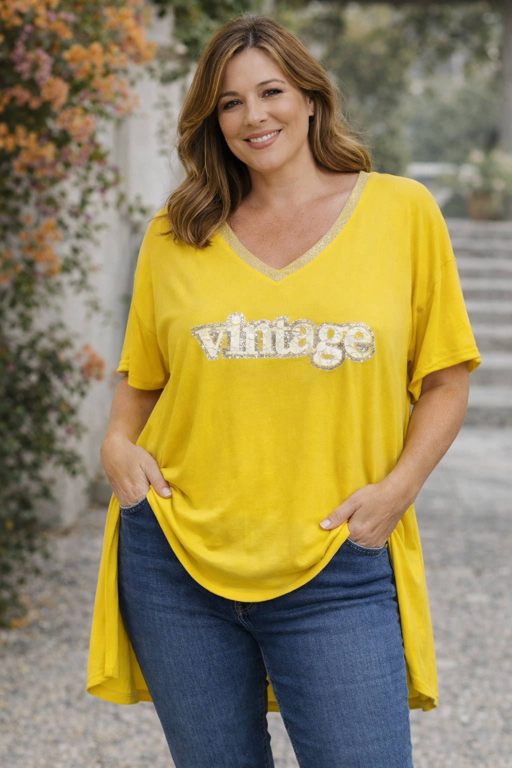 Femme blonde en t-shirt jaune “Vintage”, pose naturelle, fond flouté et lumière chaude.