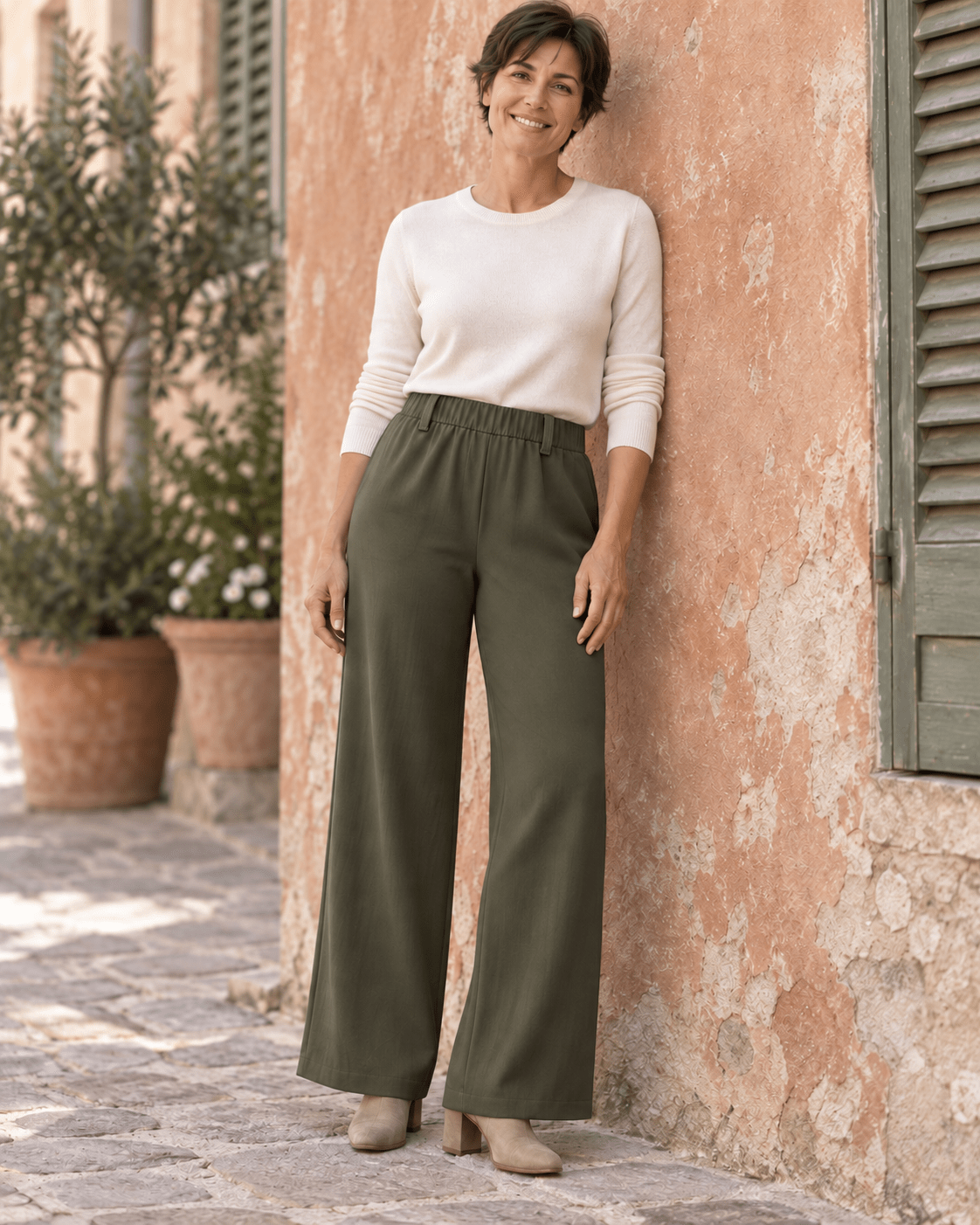 Pantalon chino kaki à jambes larges porté avec un pull ivoire devant un mur terracotta