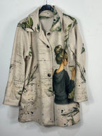 Manteau Paola beige sur cintre, femme au café et feuillage vert, vue réelle de face