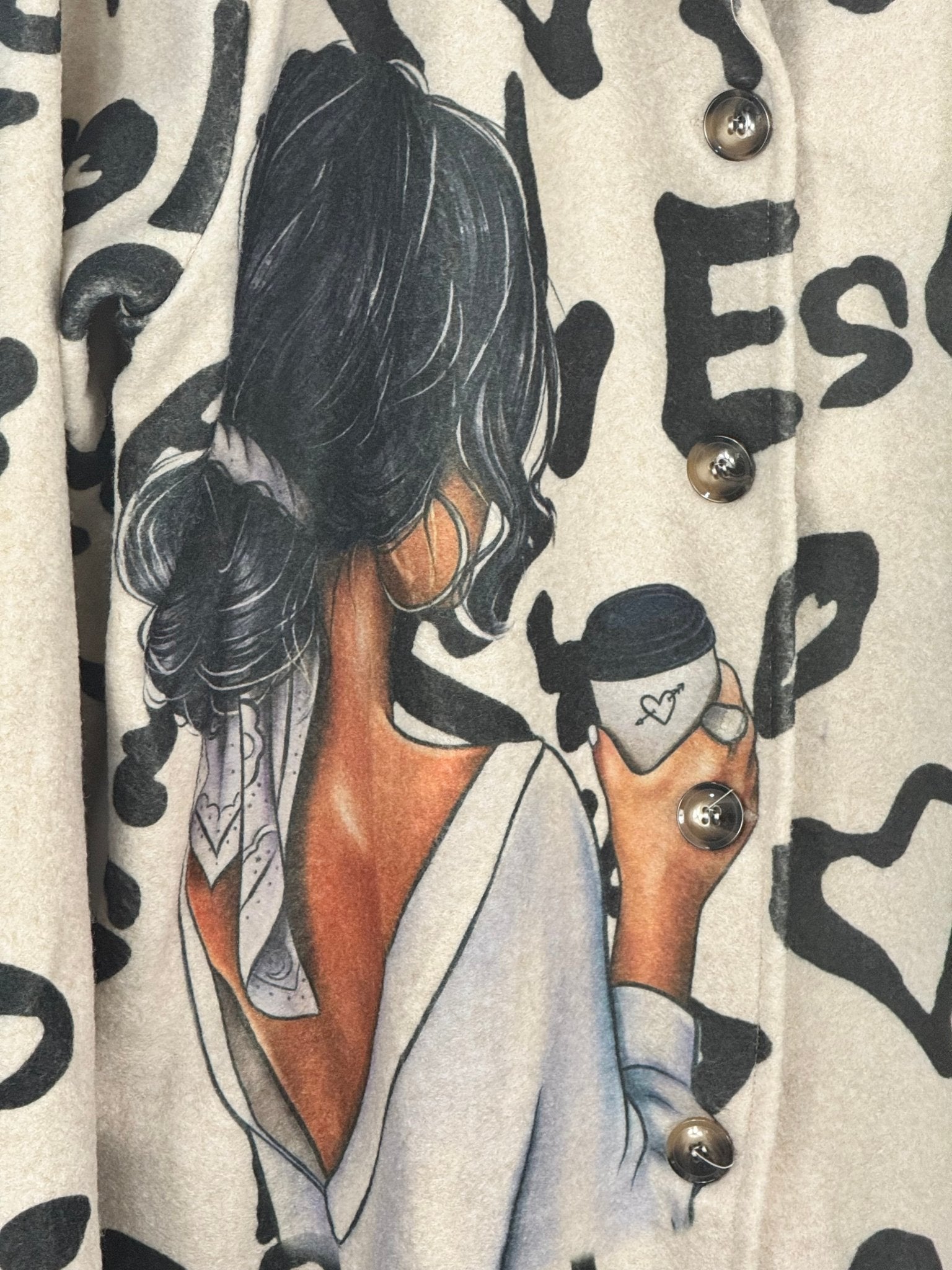 Détail réel du manteau Valentina, illustration femme au café, boutons et imprimé graphique noir