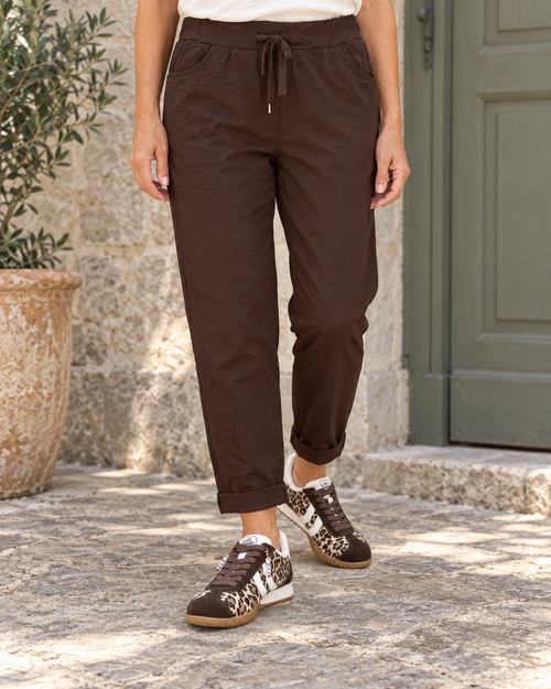 Pantalon magique Étoile chocolat porté de la taille aux pieds, avec ceinture à nouer, poches avant et baskets Louna léopard.