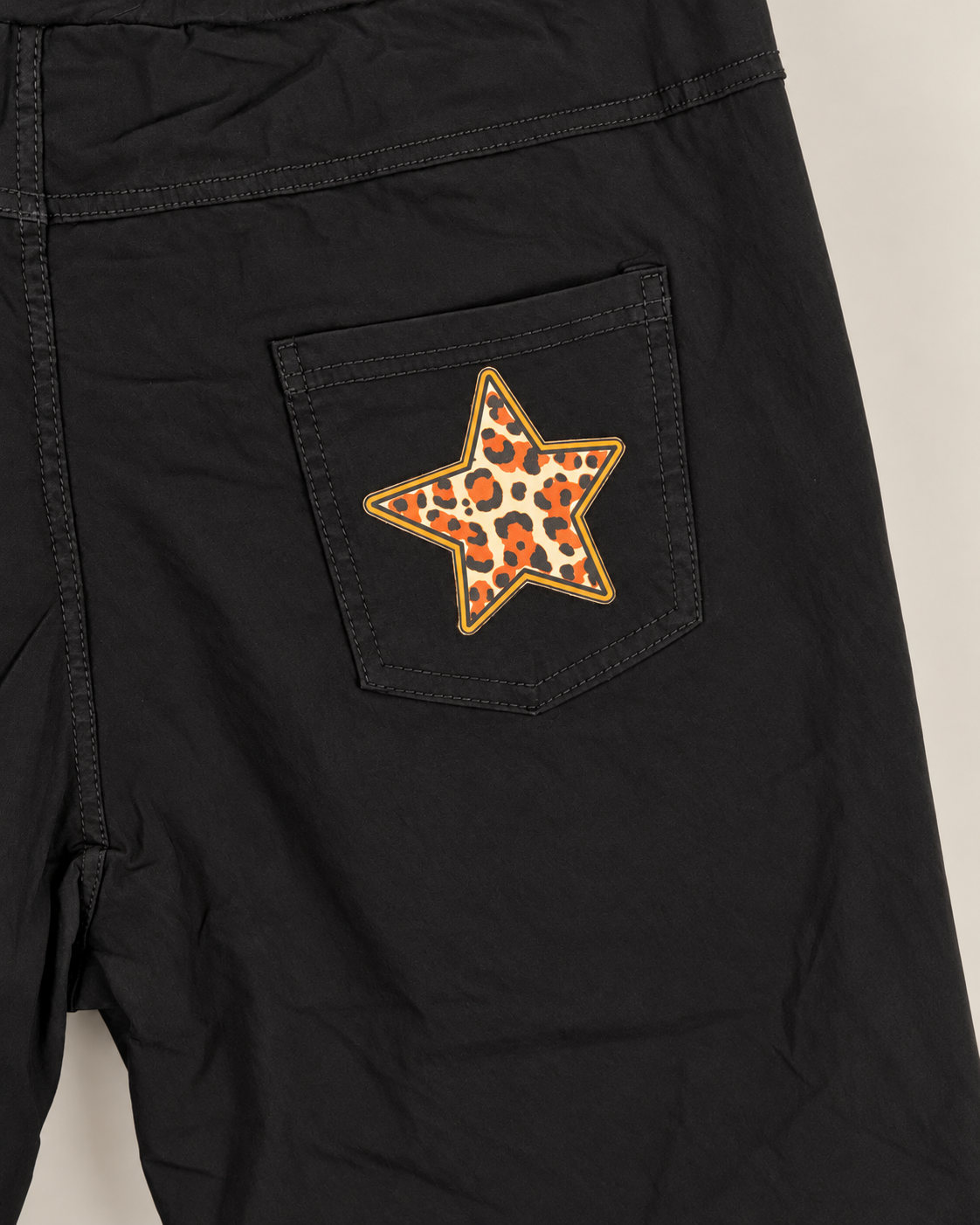 Détail retouché de la photo boutique : étoile léopard orange et noire sur la poche arrière du pantalon noir.