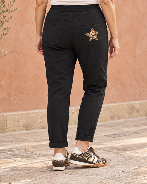 Pantalon magique Étoile noir porté de dos, deux poches plaquées et étoile léopard sur la poche arrière droite.