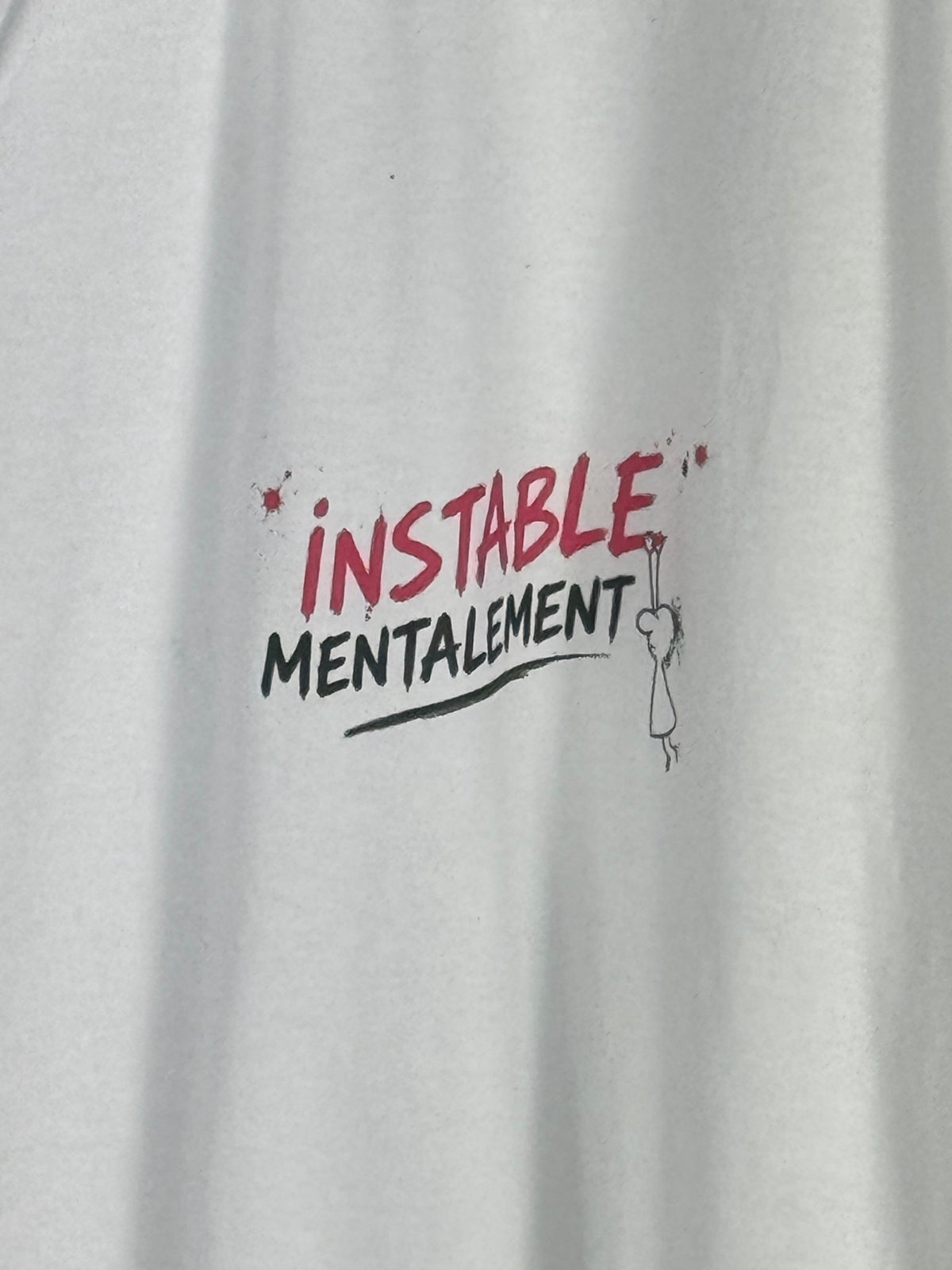 Détail du motif Instable mentalement framboise et noir sur le coton blanc du polo.