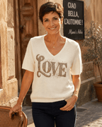 Femme portant le pull Amore blanc à motif LOVE en strass et maille baby alpaga dans une ruelle italienne automnale