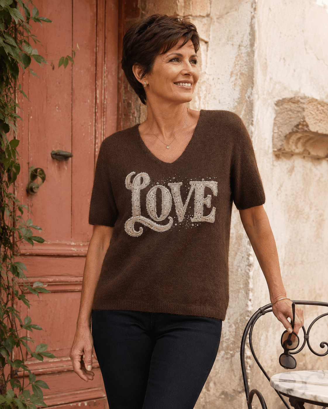 Femme portant le pull Amore chocolat à motif LOVE en strass et maille baby alpaga devant une porte terracotta en Italie