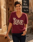 Femme portant le pull Amore lie de vin à motif LOVE en strass et maille baby alpaga devant un café italien